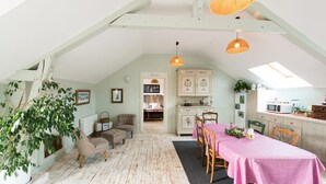 A cozy attic room with a dining table, chairs, a sofa, and a kitchen area. - 🌿 Chambres d'Hôtes Romance & PRIVATISED SPA : Intimate Luxury (Noyant-Et-Aconin)