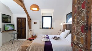 A bedroom with a bed, a television, a wooden table, a window, and a door. - 🌿 Chambres d'Hôtes Romance & PRIVATISED SPA : Intimate Luxury (Noyant-Et-Aconin)