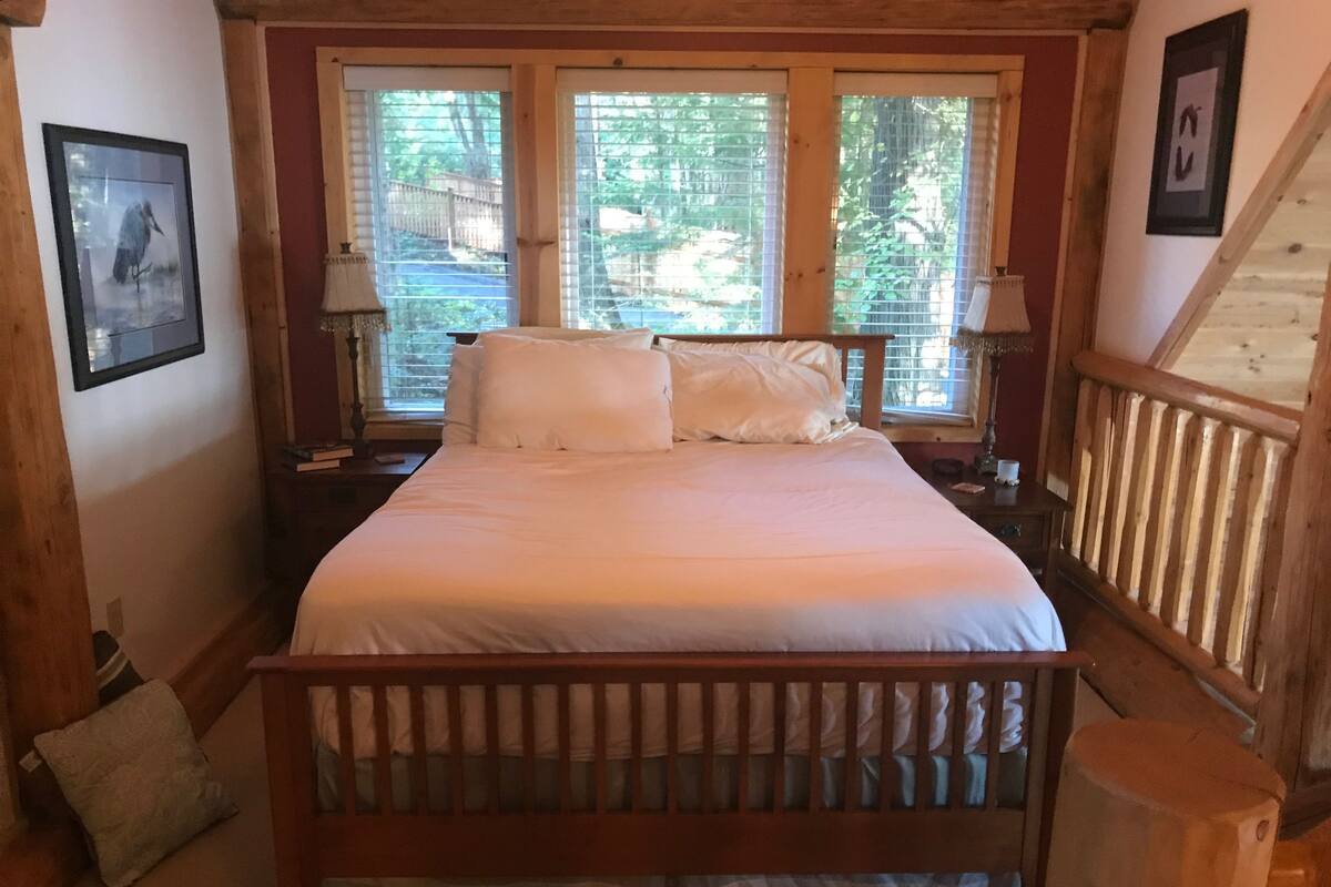 Un letto di legno con lenzuola bianche in una stanza dalle pareti e finestre in legno.
