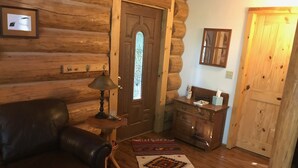 A log cabin interior with a leather sofa, a wooden table with a lamp, a wooden dresser, and a patterned rug. - The Heron House (Olympia)