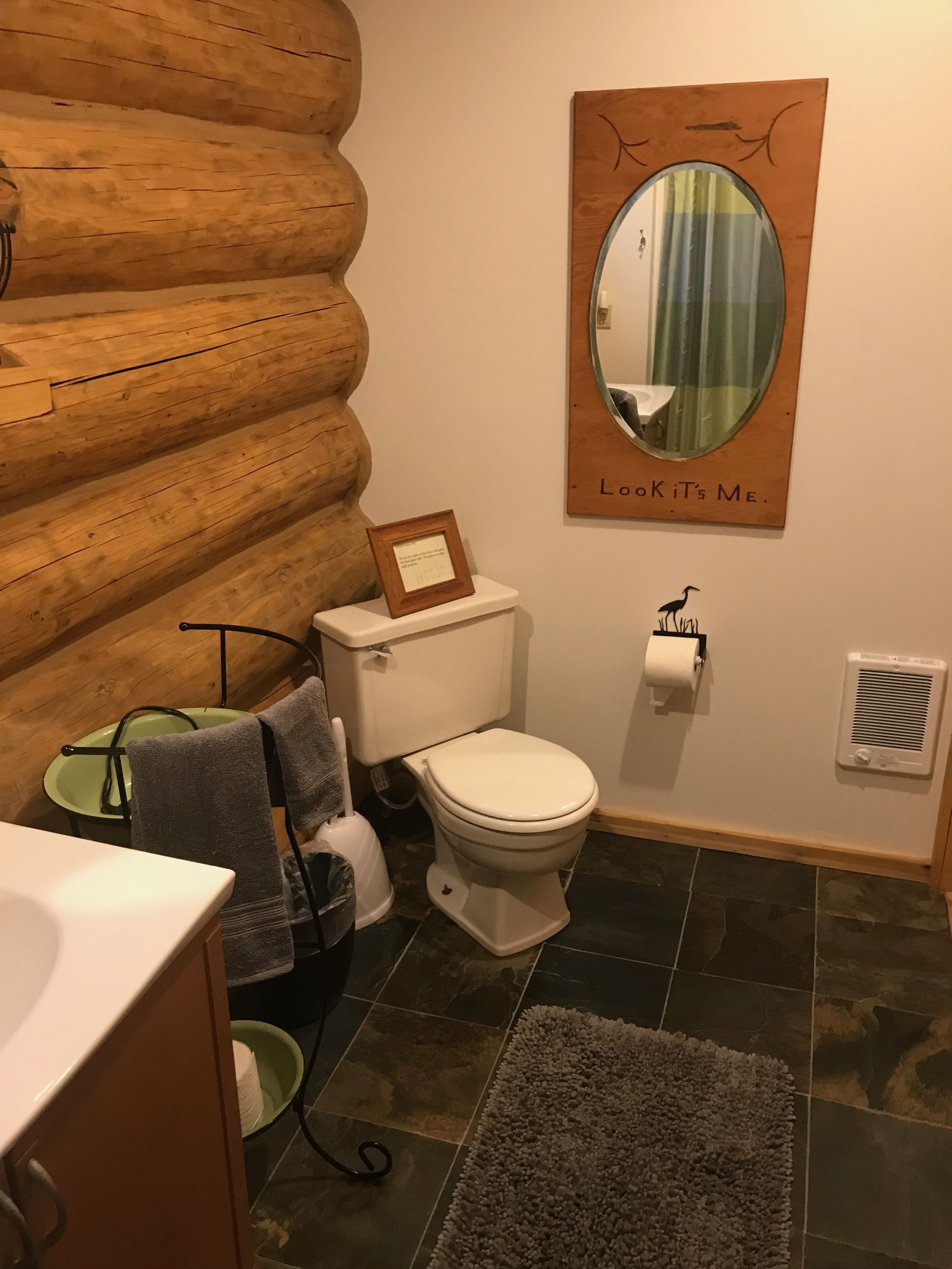 Une salle de bain avec un mur en rondins de bois, des toilettes, un lavabo, un miroir et un porte-serviettes.
