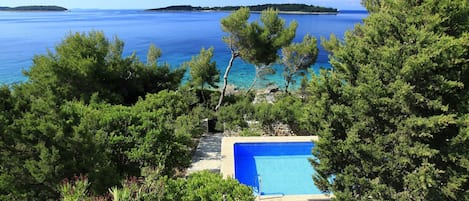 A pool surrounded by trees with a view of the sea and distant islands.