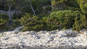 Una propietat a la costa amb un edifici de pedra, arbres i un litoral rocos.