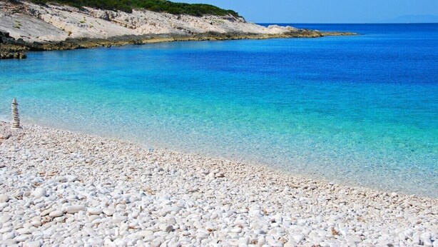Platja de còdols amb aigua turquesa cristal·lina i un litoral rocos.