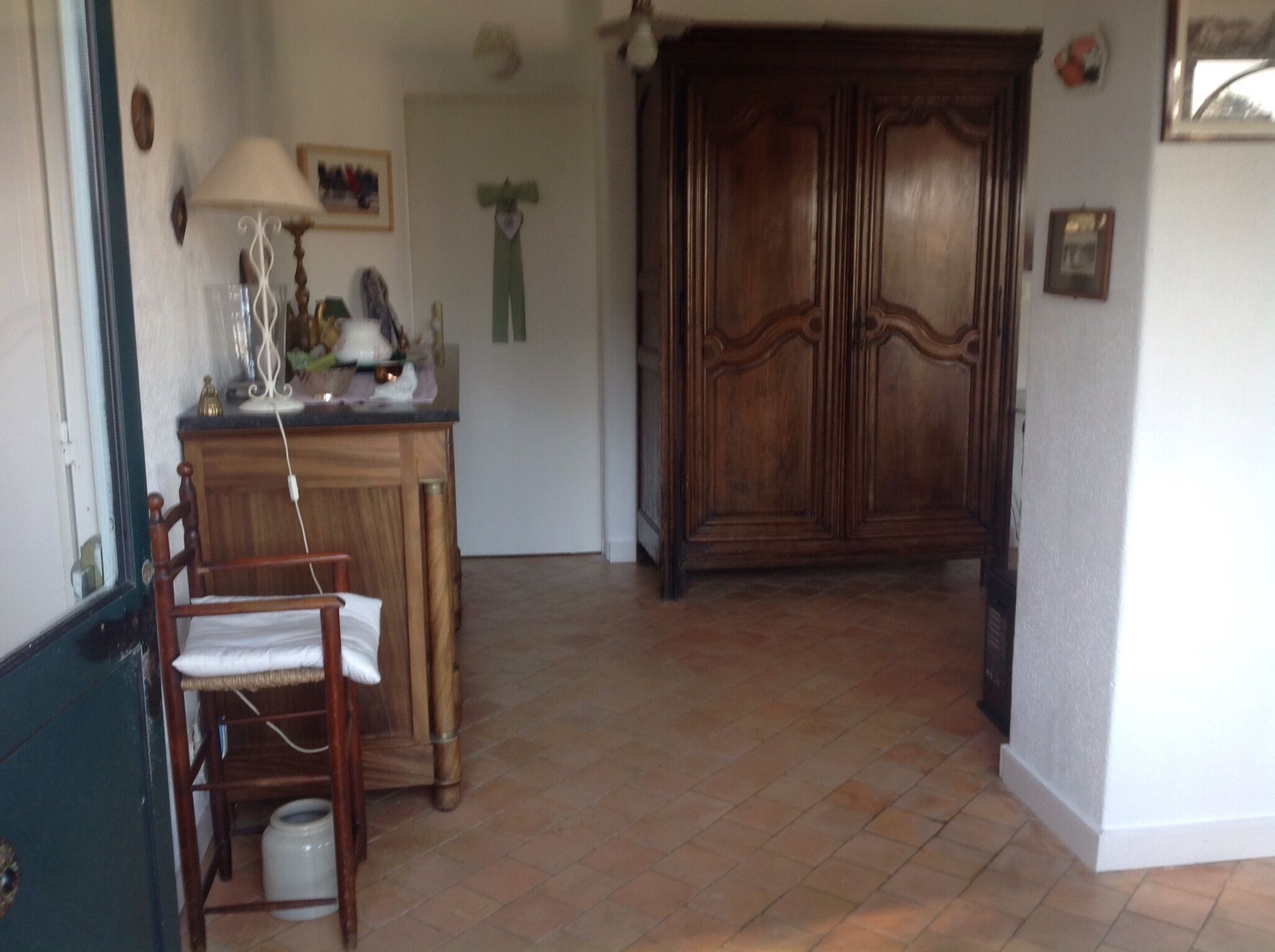 A room with a wooden cabinet, a chair, a lamp, and a tiled floor.