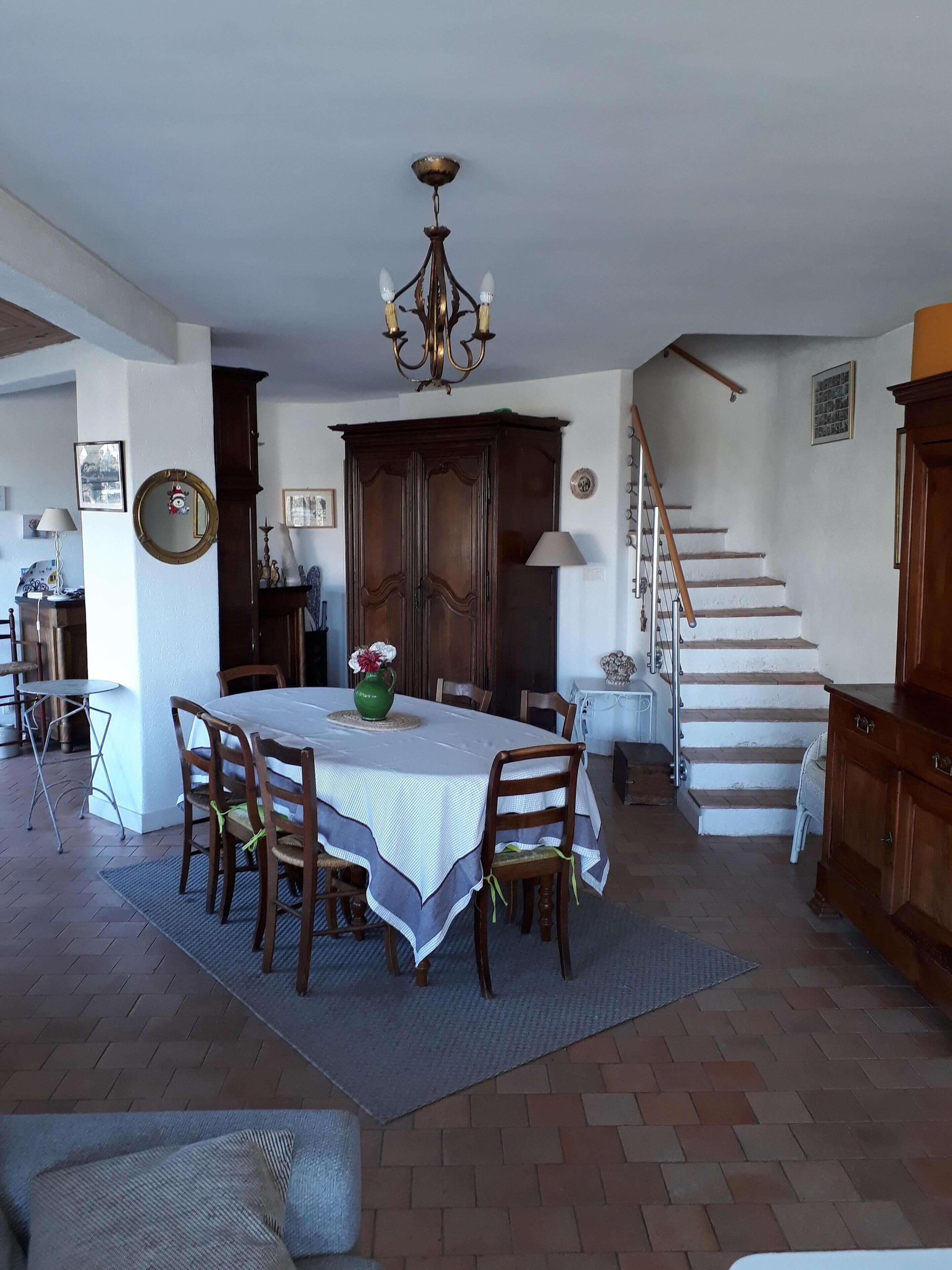 Un espace repas comprenant une table ronde, des chaises, un lustre et un escalier menant à l’étage supérieur.