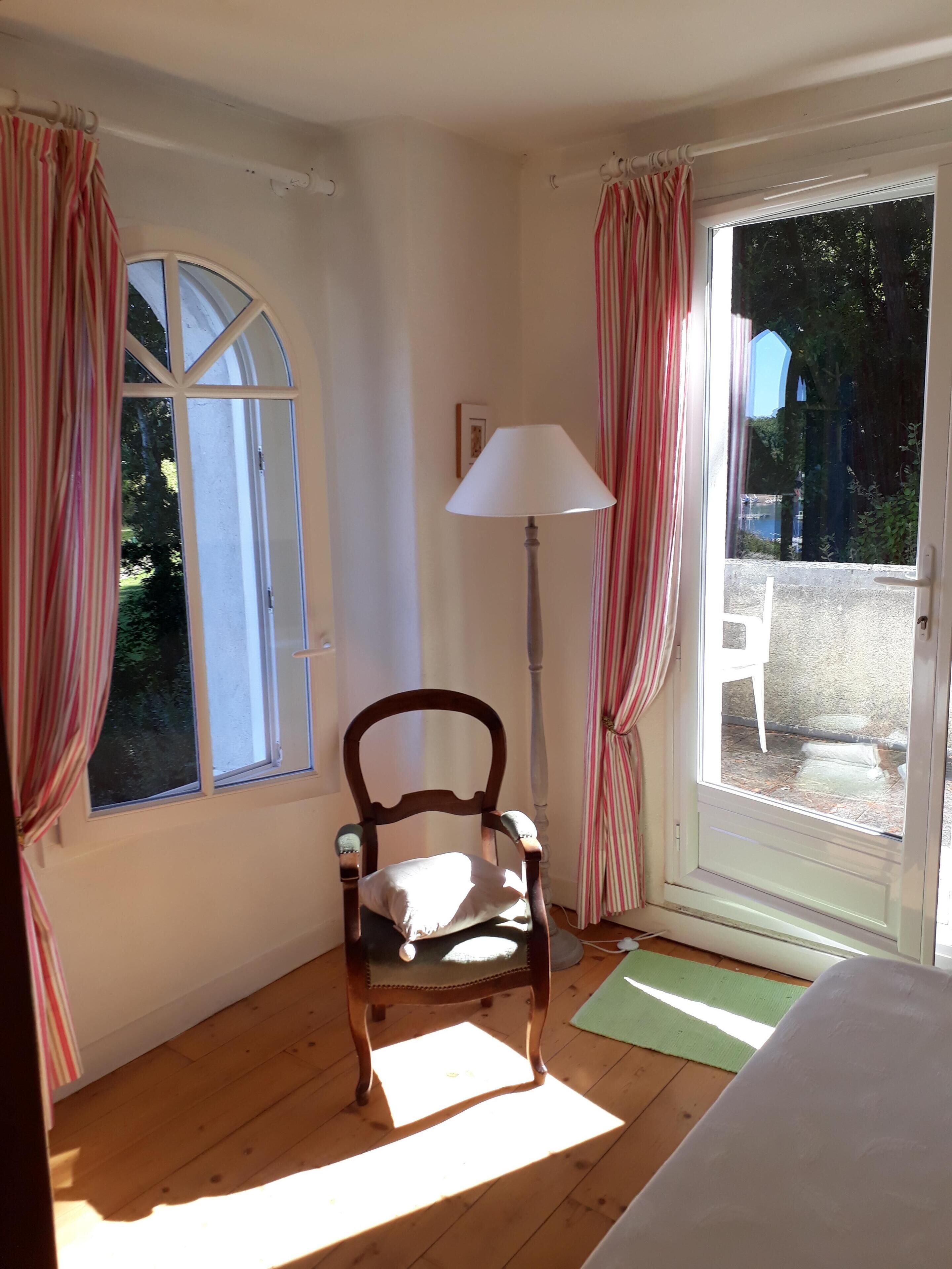 A room with a wooden chair, a lamp, and a window with curtains.