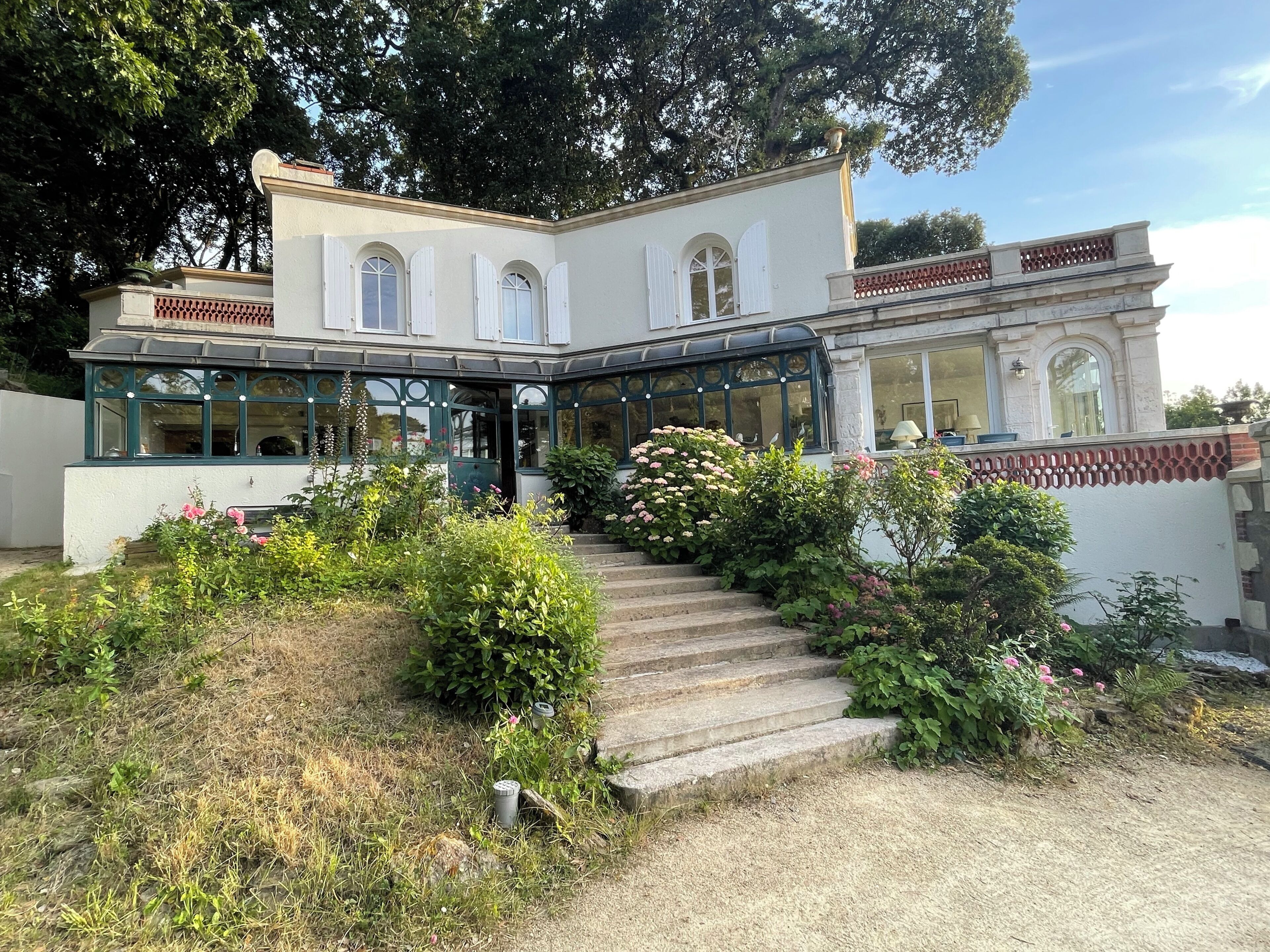 Un bâtiment à deux étages doté d’une entrée couverte, d’un jardin agrémenté de fleurs roses et d’un escalier en pierre menant à l’entrée.
