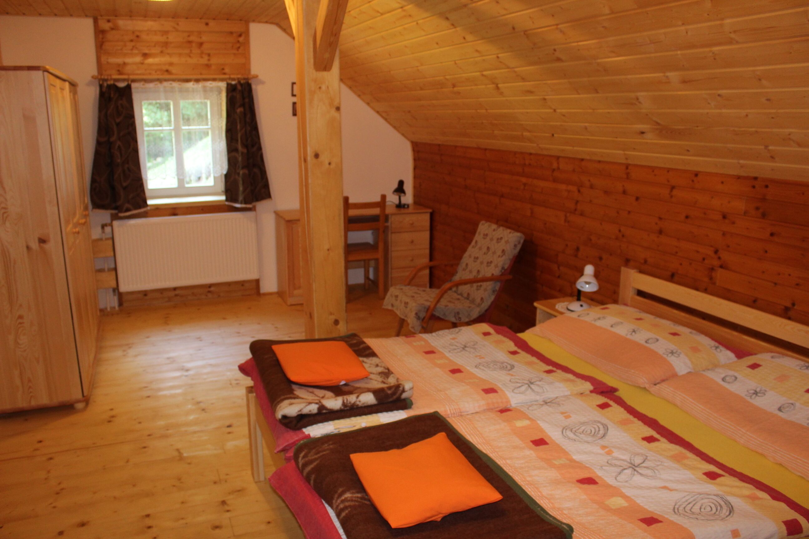 A cozy bedroom with two beds, wooden walls, a window with curtains, a chair, and a dresser.