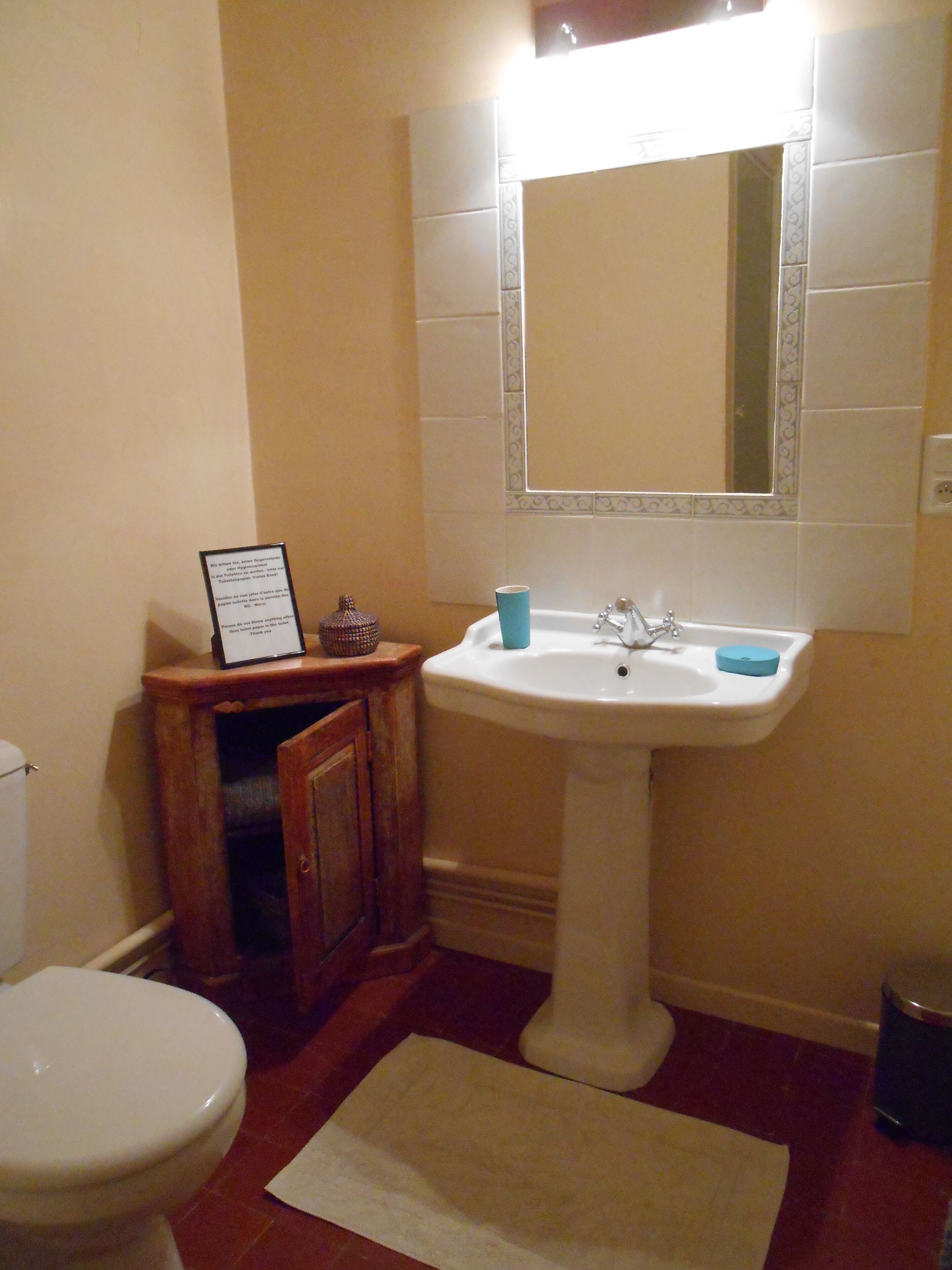 A bathroom with a pedestal sink, a mirror above it, a small cabinet, and a toilet.