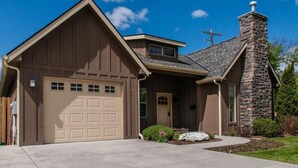 Une maison de plain-pied avec un garage, une cheminée en pierre et une pelouse bien entretenue.