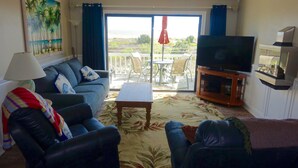 Un salon comprenant un canapé, un téléviseur, une table basse et un balcon aménagé avec du mobilier d’extérieur.