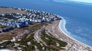 Vue aérienne d’une zone résidentielle côtière, avec des maisons le long du littoral, une plage de sable et une vue dégagée sur l’océan.