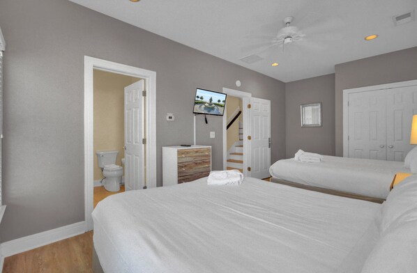 Une chambre d’hôtel avec deux lits, un téléviseur fixé au mur, une salle de bain avec des toilettes et un lavabo, et un escalier menant à une autre chambre.