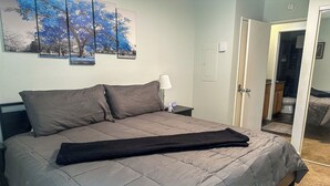 Une chambre à coucher comprenant un lit, une table de chevet, une lampe et une porte donnant sur une salle de bain.