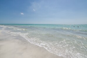 Ein Strand mit klarem Wasser und ein paar badenden Personen.
