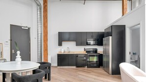 Una cocina moderna con armarios negros, microondas, horno y refrigerador. Hay una zona de comedor con una mesa y sillas blancas.