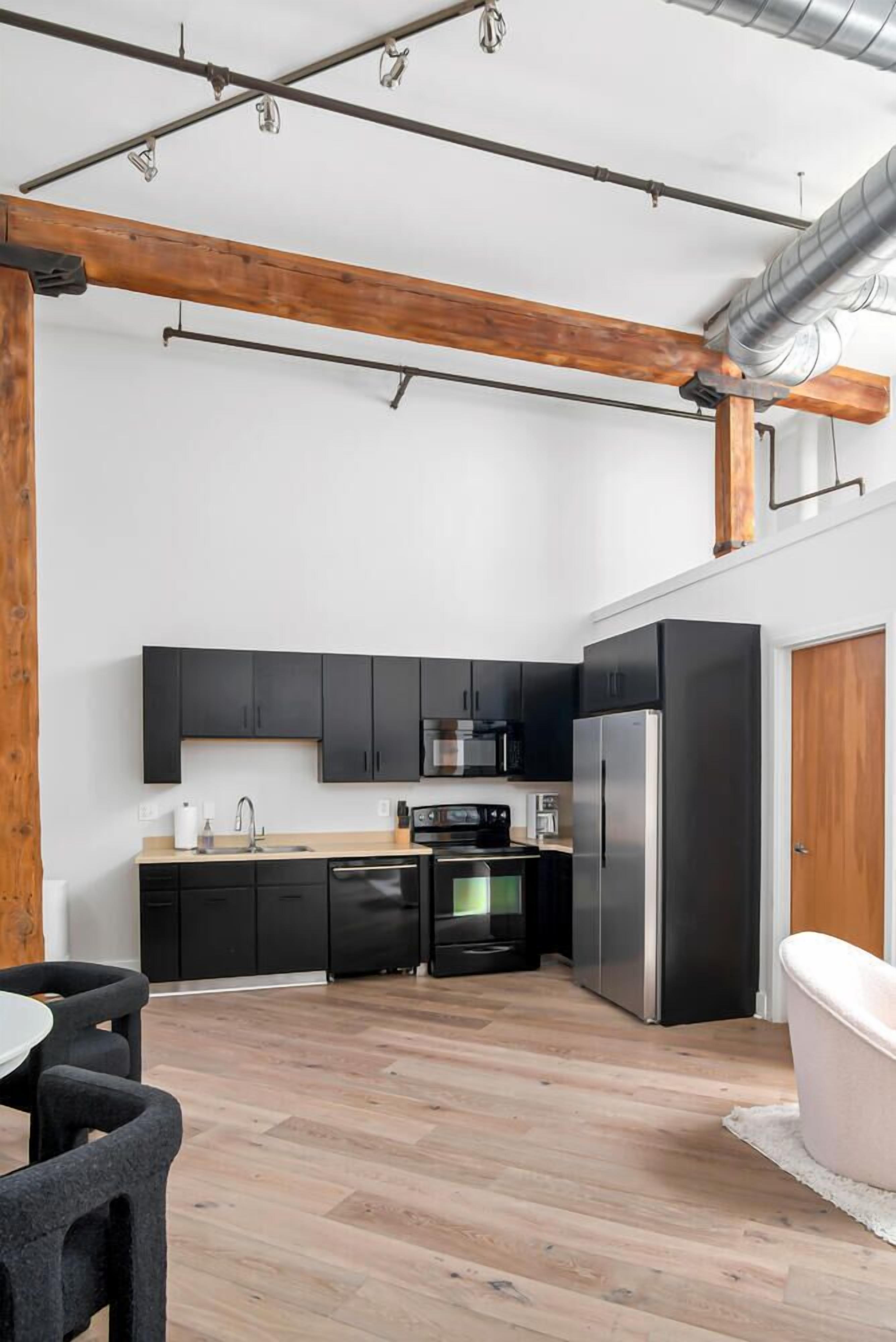 Una cocina moderna con gabinetes negros, electrodomésticos de acero inoxidable y vigas de madera a la vista.