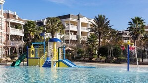 Ein Swimmingpool mit Rutsche und Wasserspielbereich, umgeben von Palmen und Hotelgebäuden.