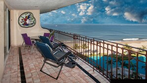 A balcony with a view of the ocean, a pool, and a tropical setting.