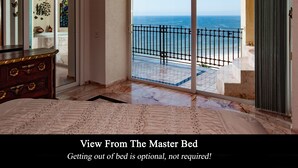 A master bedroom with a view of the ocean through a sliding glass door.