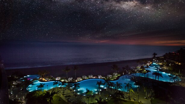 A resort with multiple swimming pools, palm trees, and a night sky with stars.