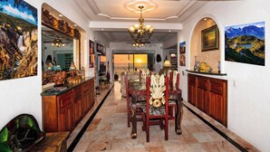 A spacious hallway with a dining area featuring ornate chairs and a chandelier.
