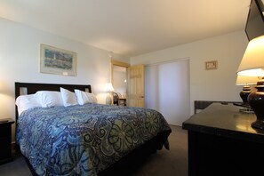 A hotel room with a bed, a desk, a chair, a lamp, and a door.
