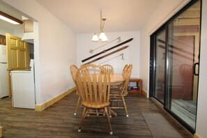 A dining area with a wooden table and chairs, a hanging light fixture, and a sliding glass door leading to a balcony.