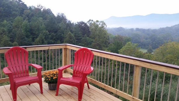 A wooden deck with two red Adirondack chairs and a small table with a potted plant.