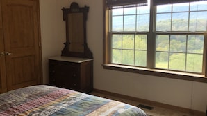A bedroom with a large window, a wooden wardrobe, and a bed with a colorful quilt.