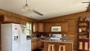 A modern kitchen with wooden cabinets, a white refrigerator, a microwave, a stove, and two bar stools.