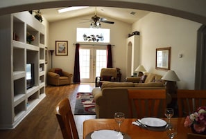 A living room with a sofa, armchairs, a dining table set for two, and a ceiling fan.