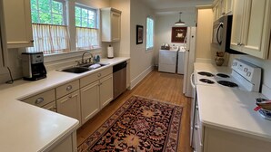 Une cuisine avec des meubles blancs, une machine à café, un lave-vaisselle, une cuisinière et un lave-linge.