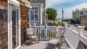 A wooden deck with a white railing, a glass door, and two wooden chairs. - Beach Block Living in Charming South Rehoboth. (Rehoboth Beach)
