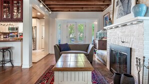 A living room with a wooden coffee table, a sofa, a fireplace, and a kitchen area in the background. - Beach Block Living in Charming South Rehoboth. (Rehoboth Beach)