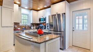 A modern kitchen with white cabinetry, stainless steel appliances, a granite countertop, and a wooden ceiling. - Beach Block Living in Charming South Rehoboth. (Rehoboth Beach)