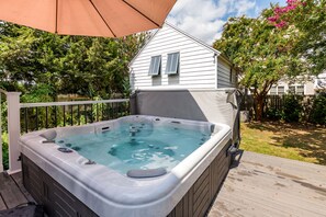 Un bain à remous sur une terrasse en bois, avec une maison en arrière-plan.