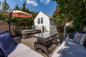 Une terrasse dotée d’une table à plateau de verre, de meubles en osier et d’un jacuzzi.