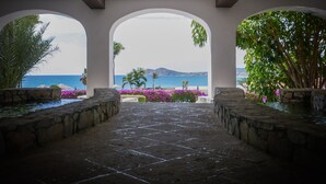 Un sendero de piedra que conduce a una zona cubierta con arcos, con vistas a una playa y montañas.