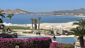 Un resort con piscina, sillas de playa, sombrillas y vistas al mar y las montañas.