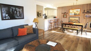 A living room with a dark grey sofa, a wooden coffee table, and a dining area with a wooden table and chairs. - Mammoth Ski & Racquet Club #114 -Pet Friendly (Mammoth Lakes)