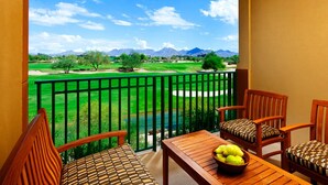 Un balcon donnant sur un terrain de golf, des meubles en bois et une table garnie de fruits.