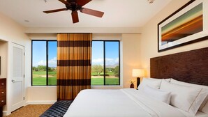 Une chambre d’hôtel avec un grand lit, un ventilateur de plafond, une vue sur un terrain de golf et un tableau au mur.