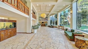 Eine geräumige Lobby mit Steinboden, Holzmöbeln und großen Fenstern, die einen Ausblick ins Freie bieten.