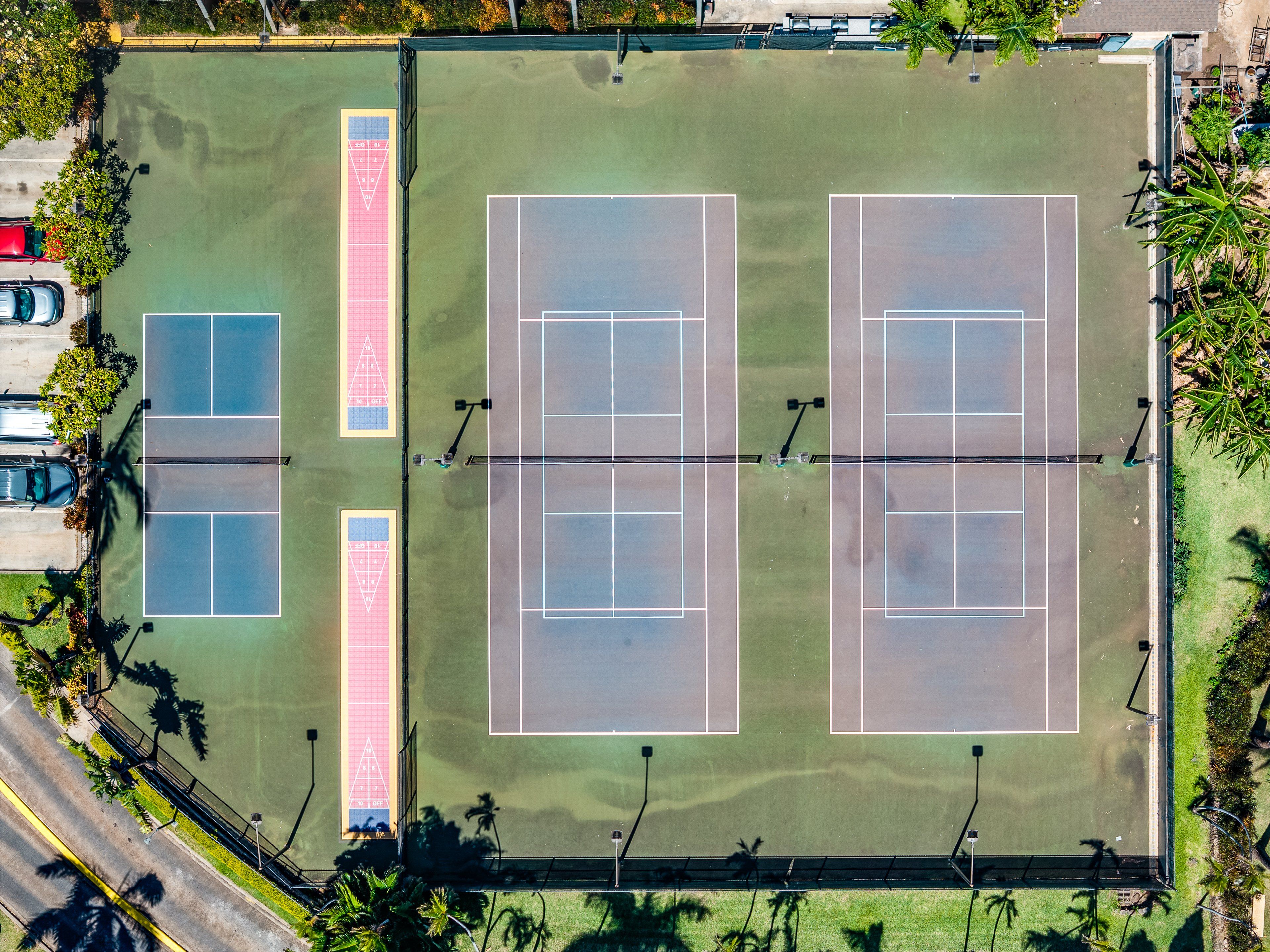 Vue aérienne d’un complexe de courts de tennis comprenant plusieurs terrains, un parking et des espaces verts environnants.