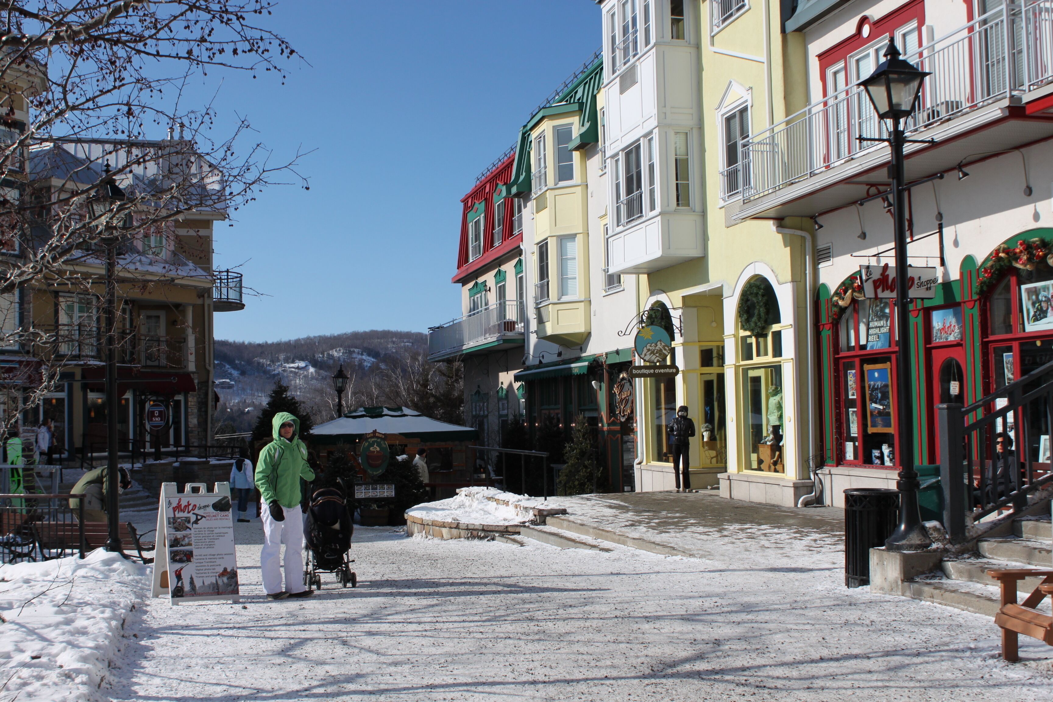 A snow-covered street with buildings, a bench, and a signboard.