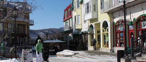 A snow-covered street with buildings, a bench, and a signboard.