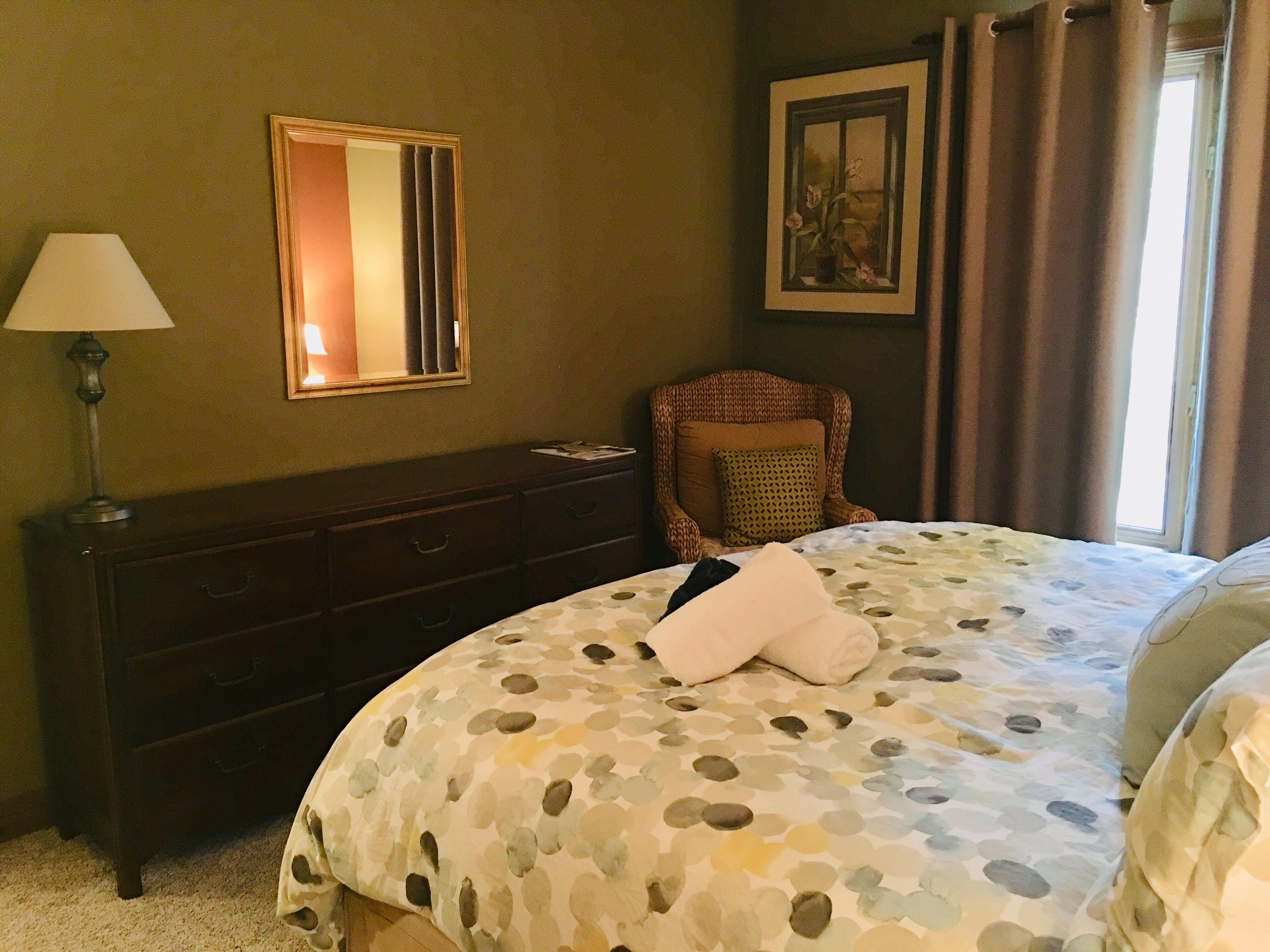 Une chambre d’hôtel avec un lit, une commode, une chaise, une lampe et un tableau au mur.