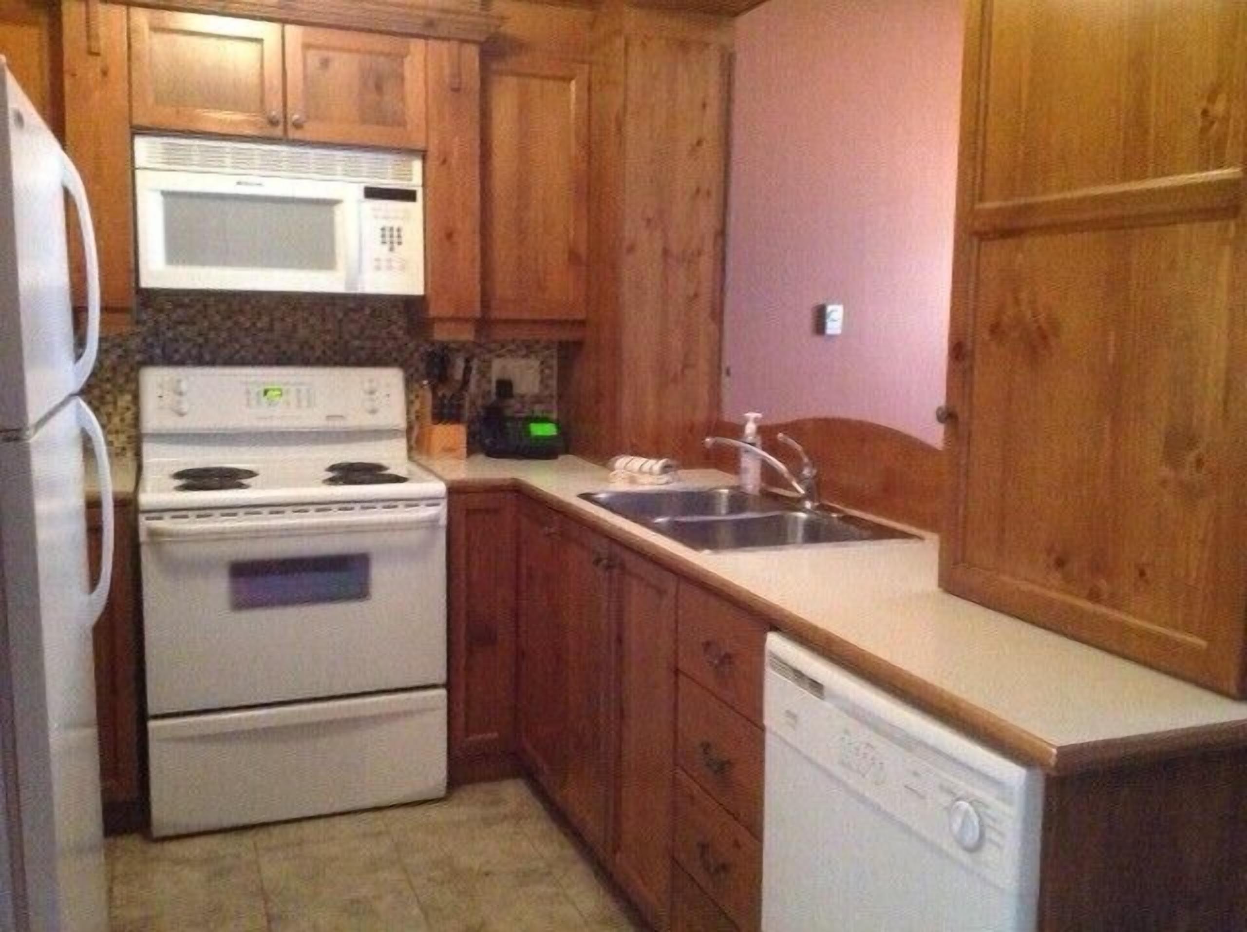 A compact kitchen with wooden cabinets, a microwave, stove, sink, and dishwasher.